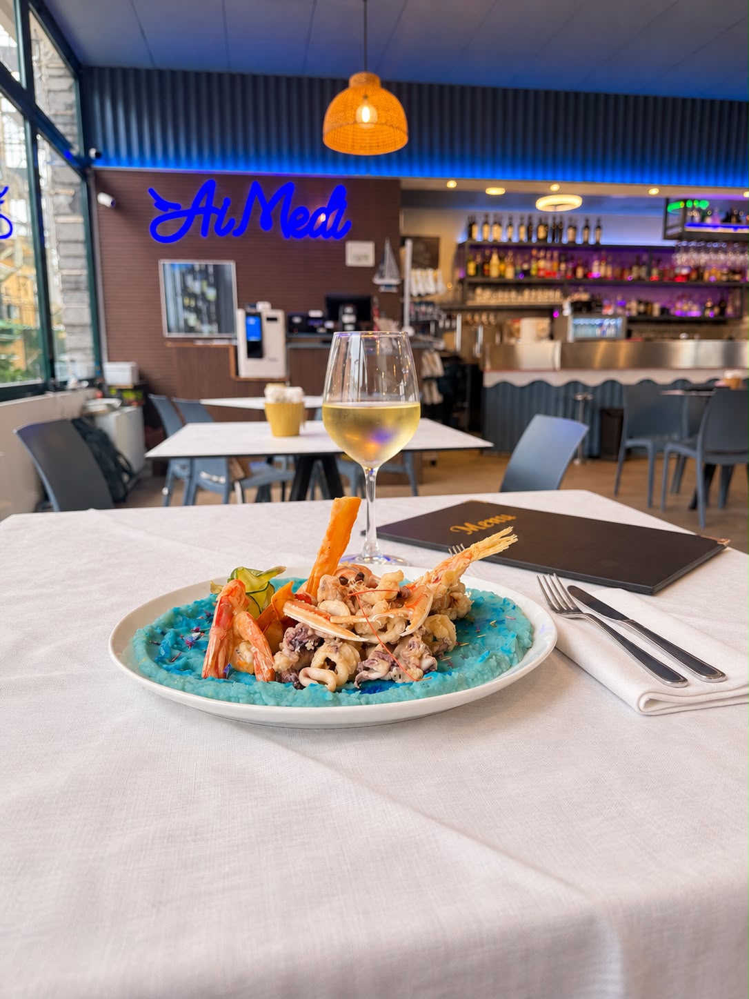 Un piatto della cucina Ai Medi, con un calice di vino e il locale sullo sfondo